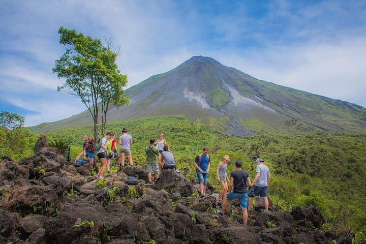 Arenal Volcano rising green above a lava field under blue sky
